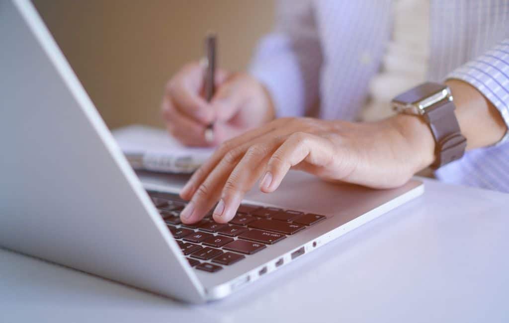 Persona escribiendo en un ordenador portátil y tomando notas para preparar un artículo de opinión